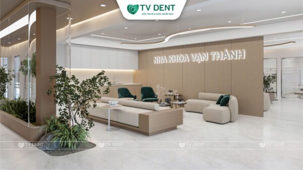 Sảnh phòng chờ Nha khoa Vạn Thành với tường ốp gỗ, logo phòng khám, sofa tông be và bồn cây xanh, thiết kế bởi TVDENT